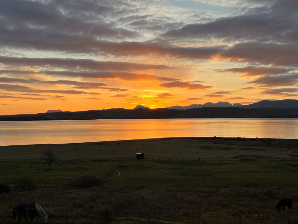 A sunset over a lake with mountains in the distance and a grassy field with grazing animals at Calmdale in Inverasdale near Poolewe