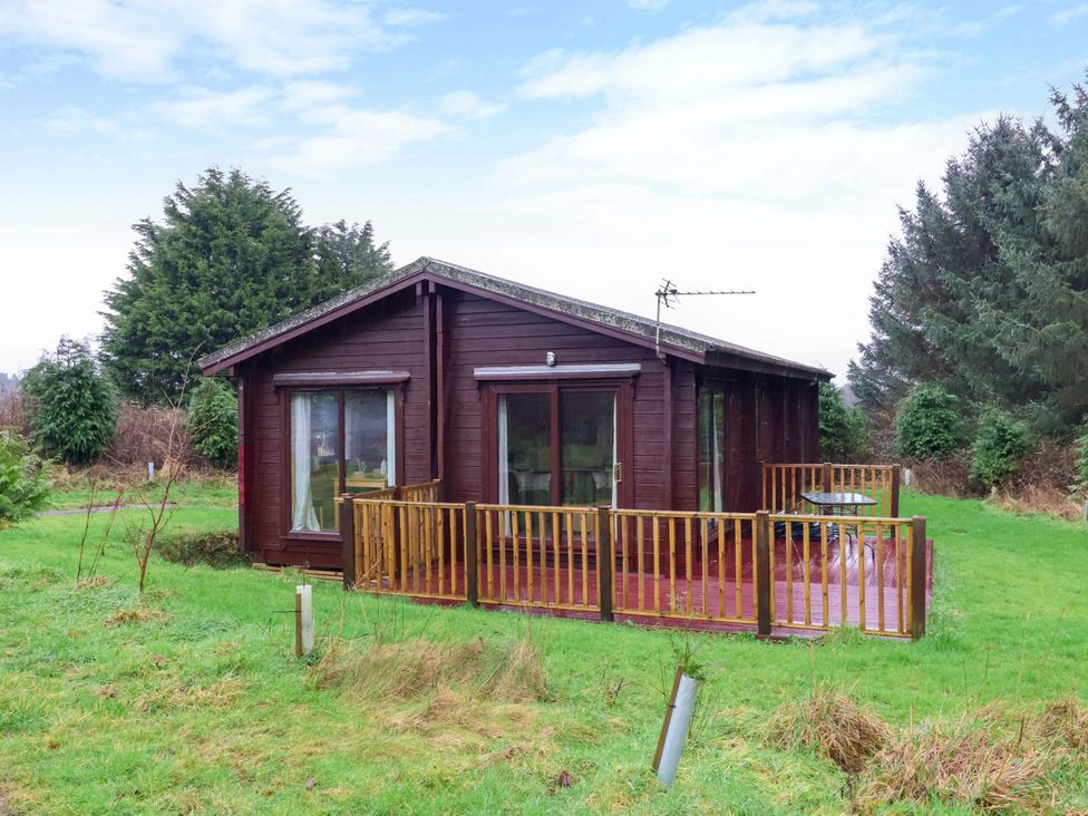 A cabin with a deck surrounded by grass and trees at Elderberrys Lodge in Bideford