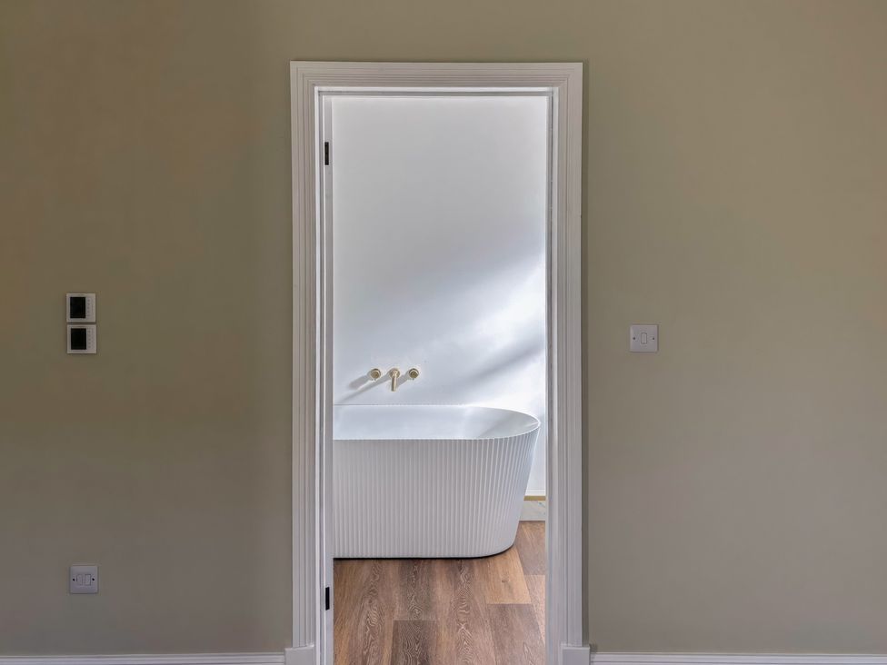 A bathroom with a bathtub visible through the door at Holt Hall - Ground Floor Apartment in Matlock