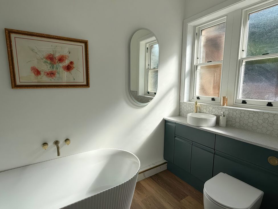 A bathroom with a bathtub, toilet, sink, and mirror at Holt Hall - Ground Floor Apartment in Matlock