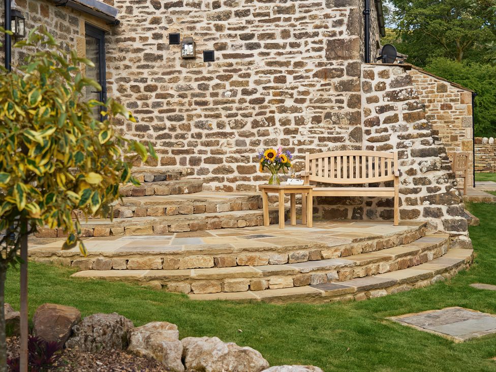 An outdoor area with a wooden bench and flowers near a stone wall at The Reading Rooms in Oughtershaw near Buckden