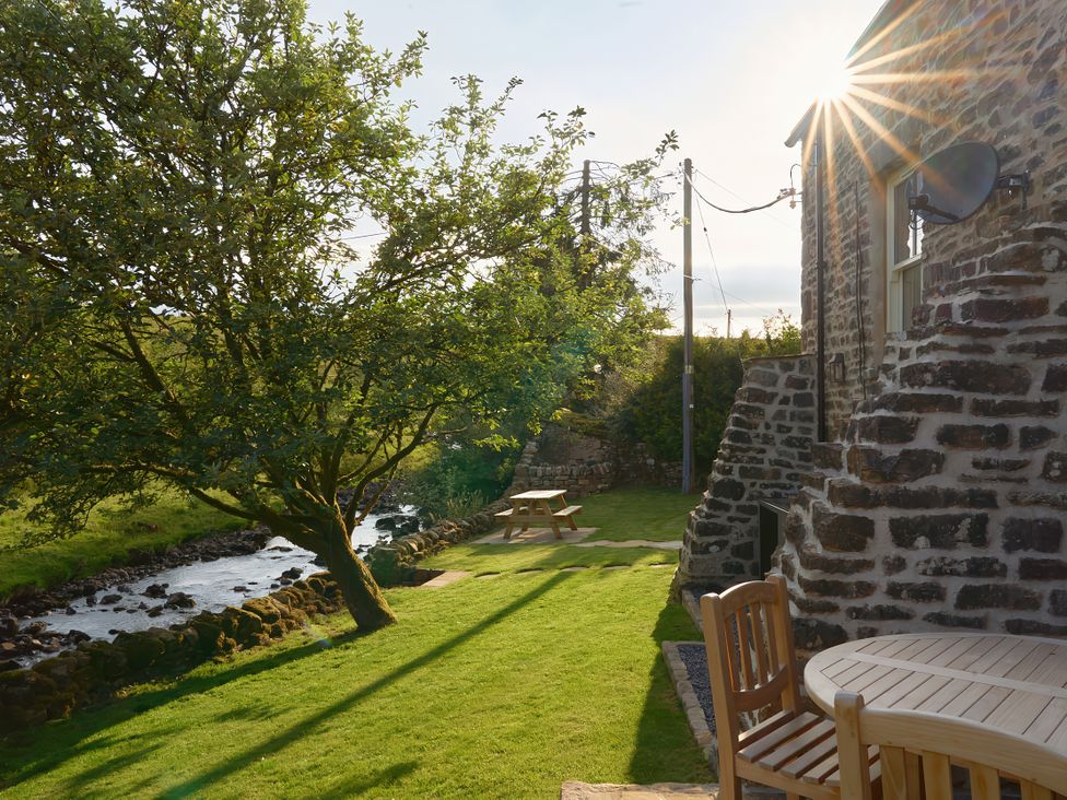 An outdoor area with a tree and picnic table by a stream at The Reading Rooms Oughtershaw near Buckden
