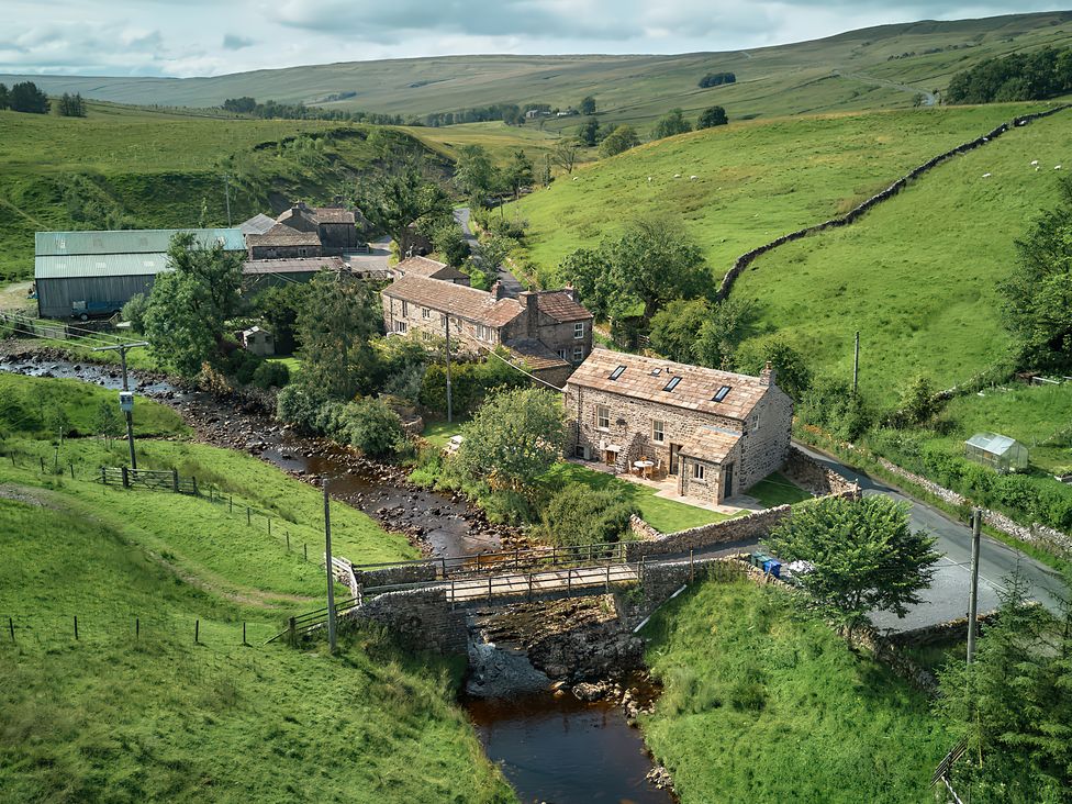 An aerial view of buildings and a bridge over a stream at The Reading Rooms Oughtershaw near Buckden