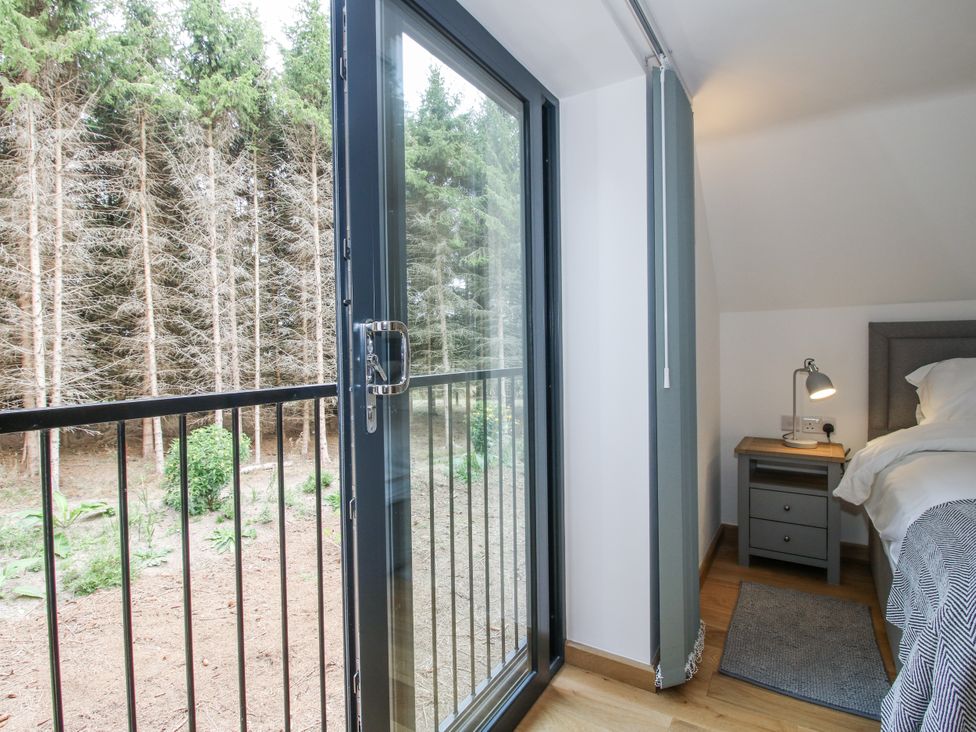 A bedroom with a balcony door and side table at The Barn in Acton near Bishop's Castle