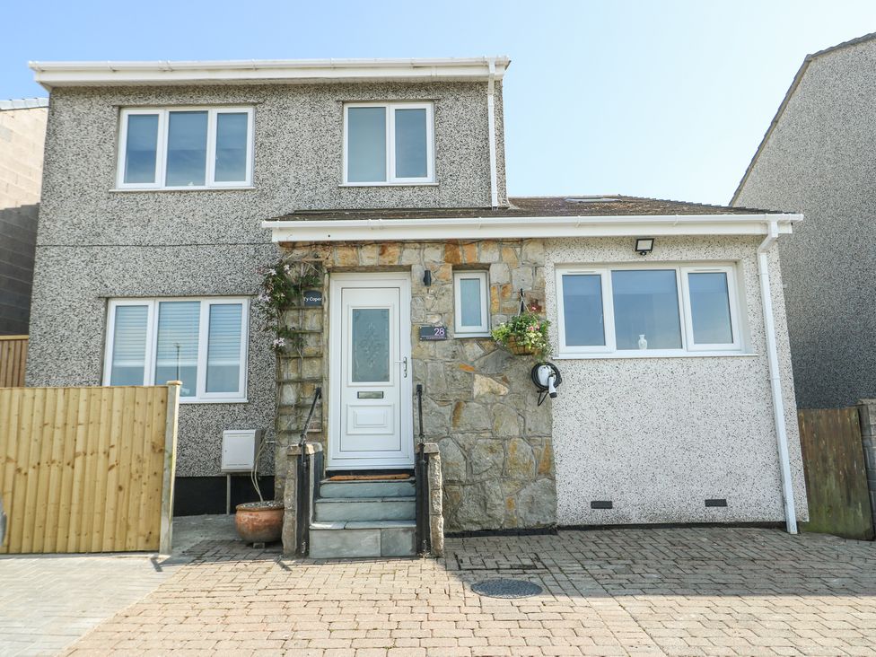 The front view of a two-story house with multiple windows a white door stone and pebble dash exterior and a driveway at Ty Copr in Amlwch