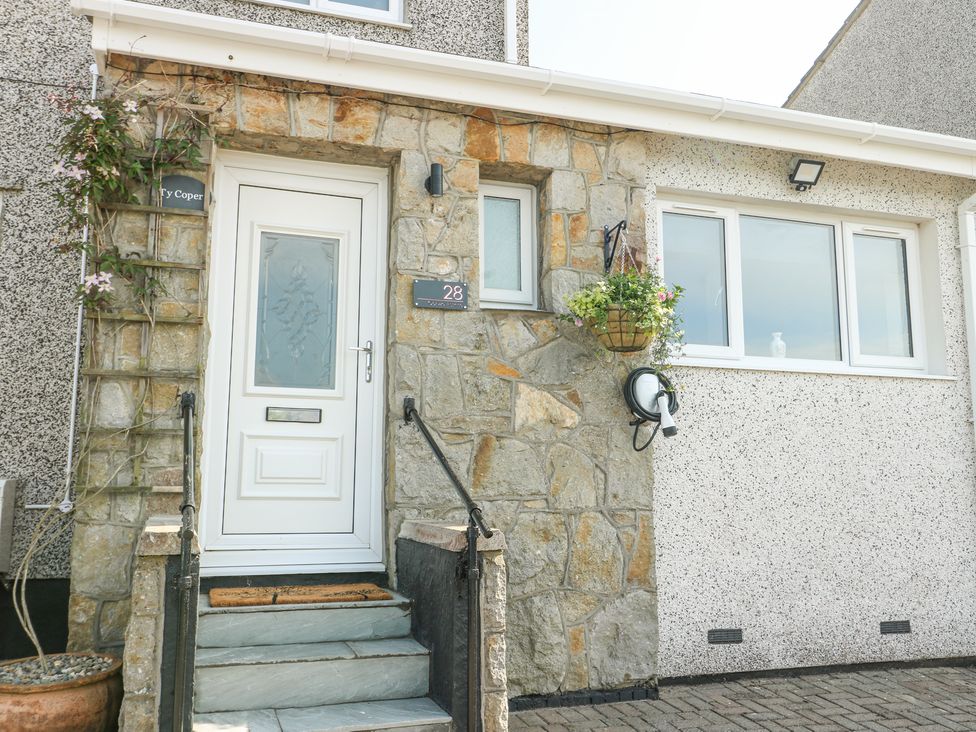 Front entrance of a house with a white door stone steps and a hanging flower pot at Ty Copr in Amlwch