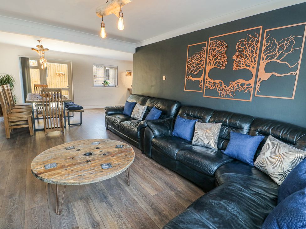 A living room with black leather sofas and a round wooden coffee table and a wooden dining table with chairs at Ty Copr in Amlwch