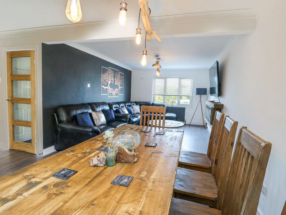 A living room with wooden dining table and chairs a black leather sofa and wall-mounted tv at Ty Copr in Amlwch