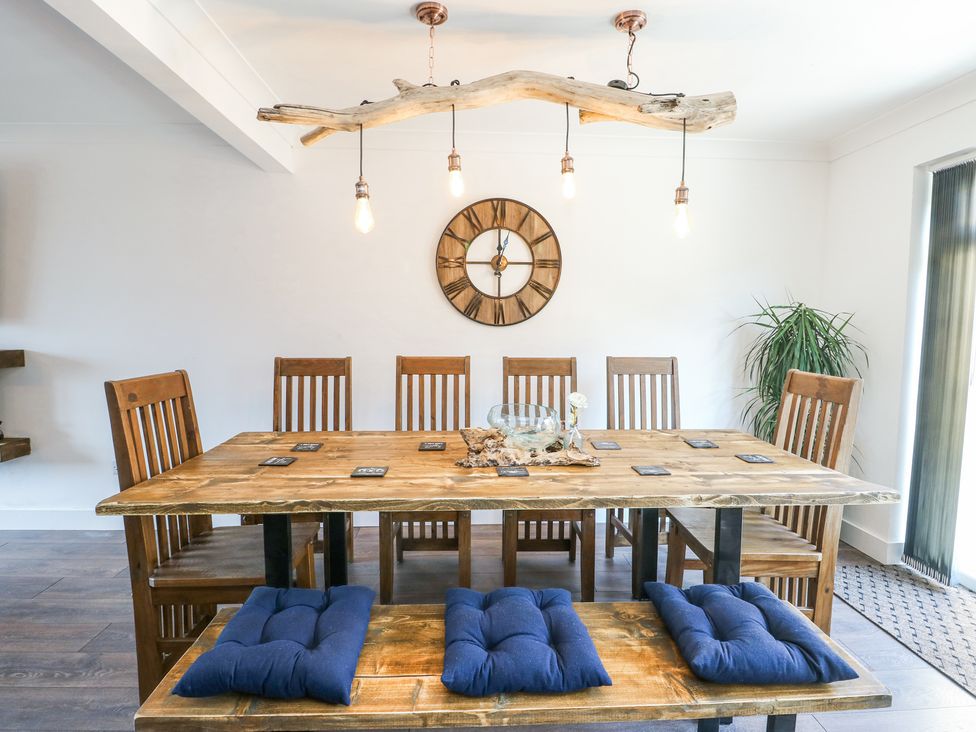 A dining room with a wooden table and chairs with blue cushions and a wooden clock on the wall at Ty Copr in Amlwch