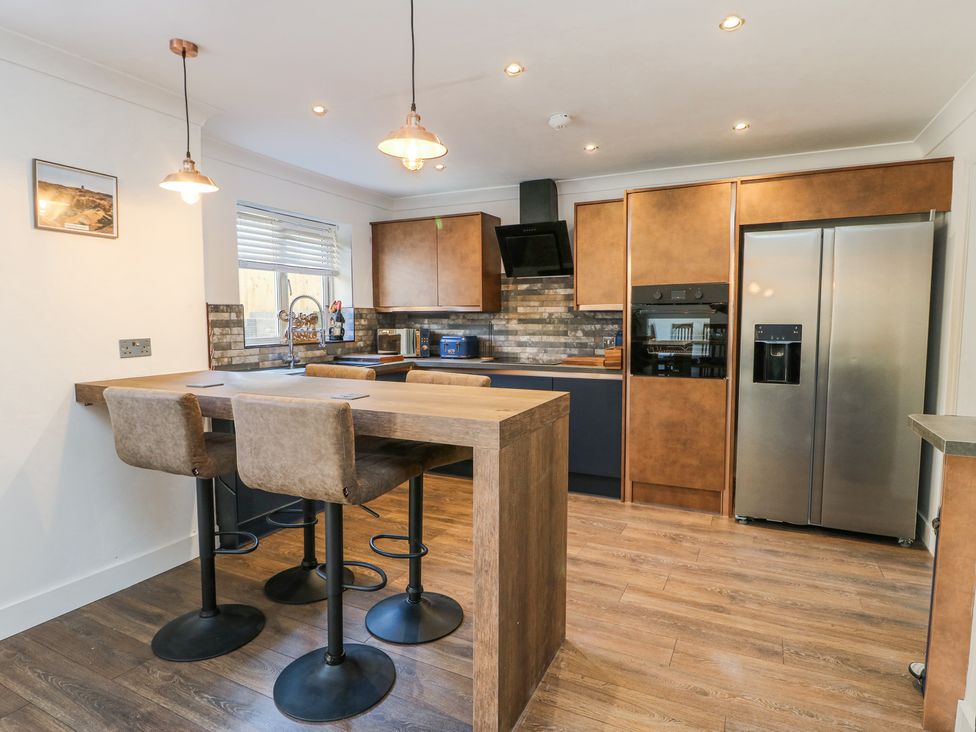 A kitchen with wooden cabinets a kitchen island with three stools and a stainless steel refrigerator at Ty Copr in Amlwch
