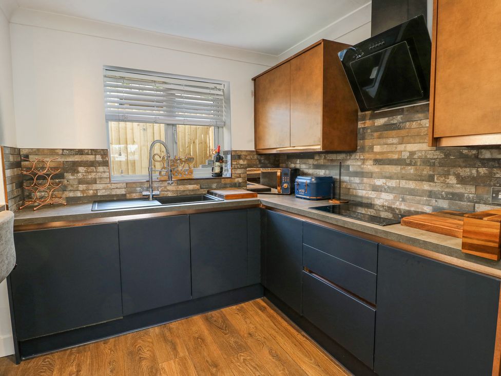 A kitchen with black lower cabinets wooden upper cabinets and a brick backsplash at Ty Copr in Amlwch