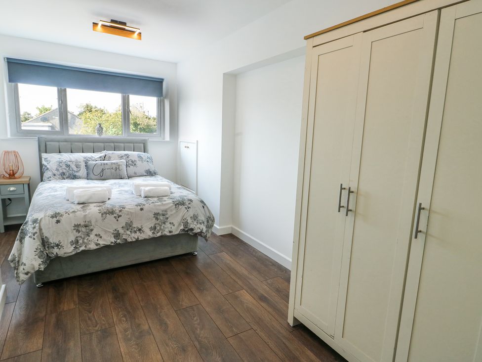 A bedroom with a double bed with floral bedding two towels on the bed a bedside table with a lamp and a wardrobe at Ty Copr in Amlwch