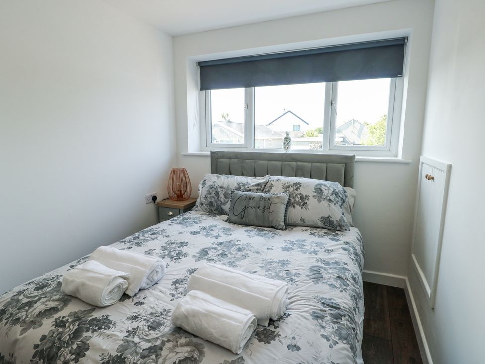 A bedroom with a double bed with floral bedding and towels on top a window with a blind and a bedside table with a lamp at Ty Copr in Amlwch