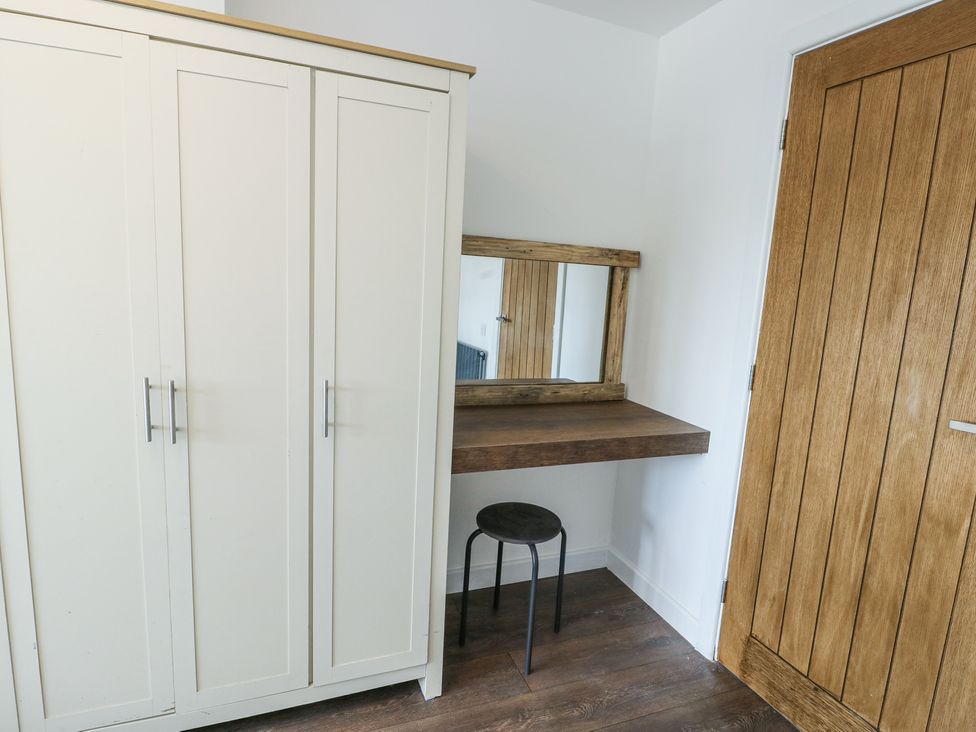 A room corner with a white wardrobe a wooden floating desk with a mirror and a black stool at Ty Copr in Amlwch