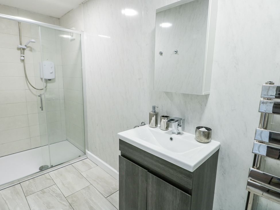 A bathroom with a glass enclosed shower on the left a sink with a cabinet and a wall mirror above at Ty Copr in Amlwch