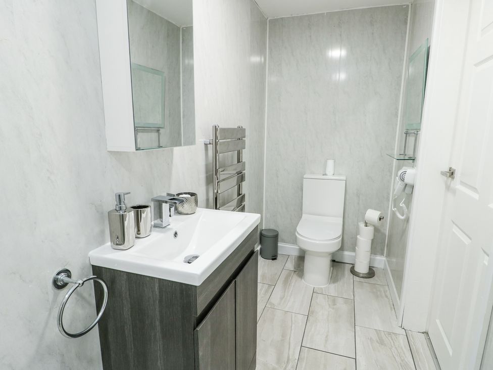 A bathroom with a sink and cabinet unit a toilet and a wall-mounted hairdryer at Ty Copr in Amlwch