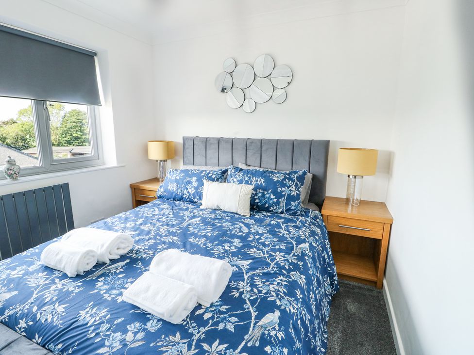 A bedroom with a bed with blue floral bedding two wooden bedside tables with lamps and a window with a closed blind at Ty Copr in Amlwch