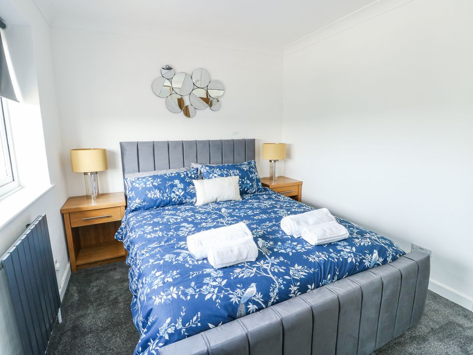 A bedroom with a bed with blue floral bedding two bedside tables with lamps and a decorative mirror on the wall at Ty Copr in Amlwch