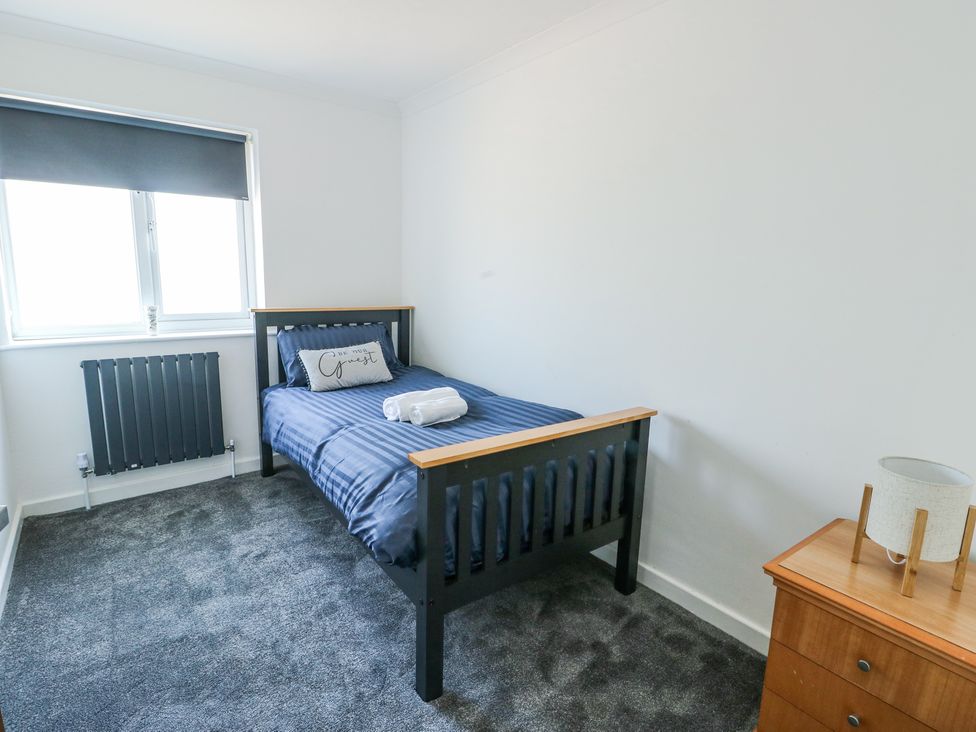 A bedroom with a single bed with navy bedding a nightstand with a lamp a window with a blind and a radiator at Ty Copr in Amlwch