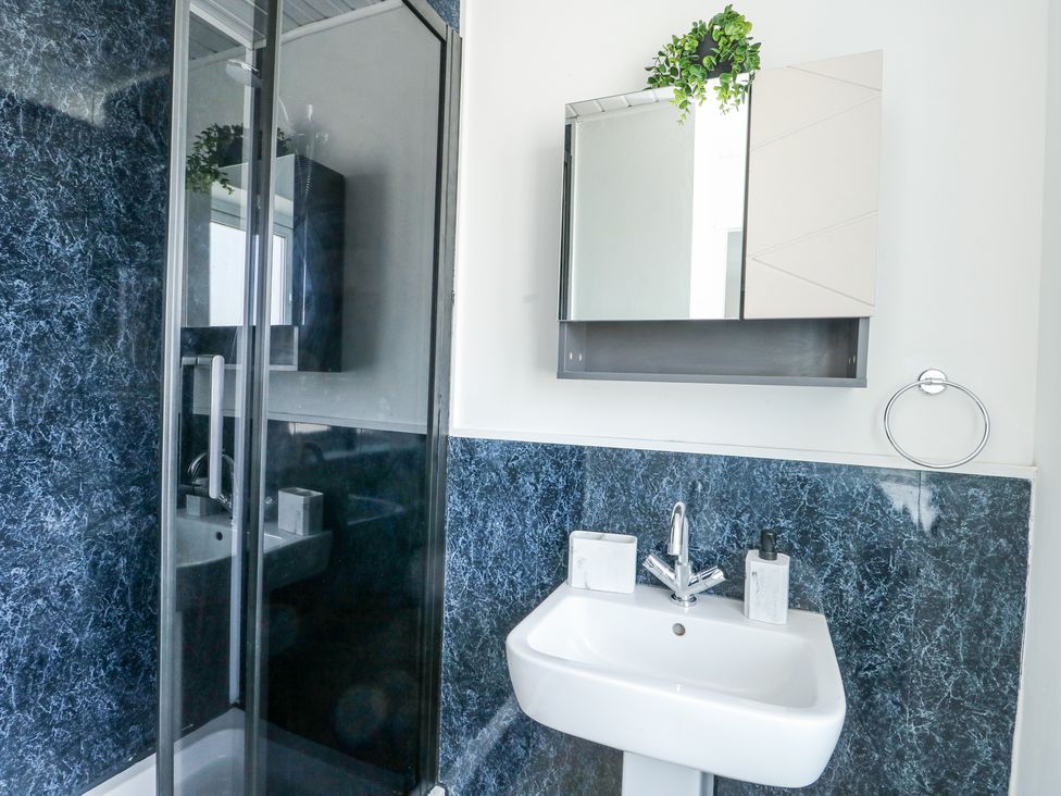 A bathroom with a white sink, a wall-mounted mirror cabinet with a plant on top, and a glass shower enclosure with dark blue marbled walls at Ty Copr in Amlwch