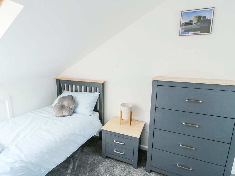 A bedroom with a single bed a bedside table with a lamp a chest of drawers and a framed picture on the wall at Ty Copr in Amlwch