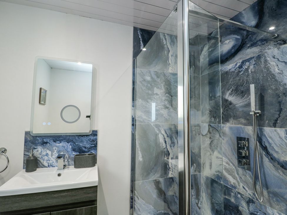 A bathroom with a white sink and a mirror above it with blue marble tiles behind and a glass shower enclosure with blue marble tiles