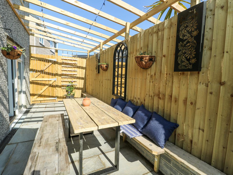 An outdoor seating area with a wooden table and benches under a wooden pergola at Ty Copr in Amlwch