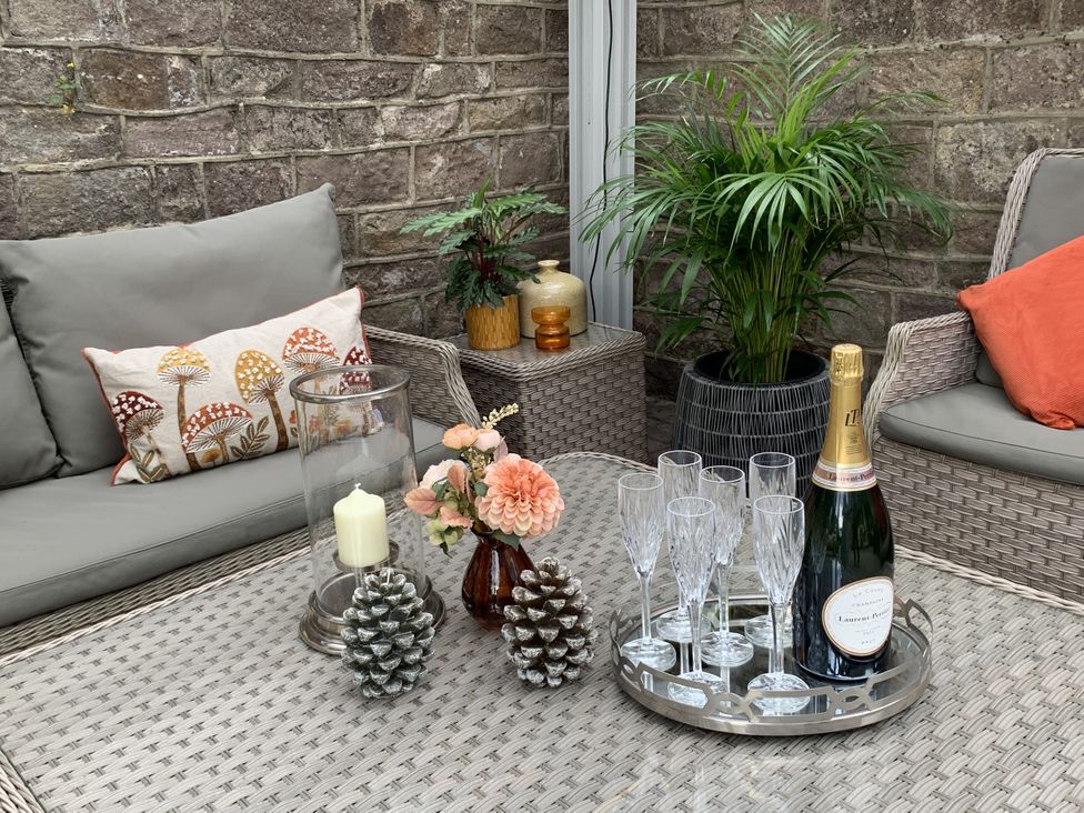 A table with glasses, a bottle, and decorative items in a conservatory at The Coach House in Holloway