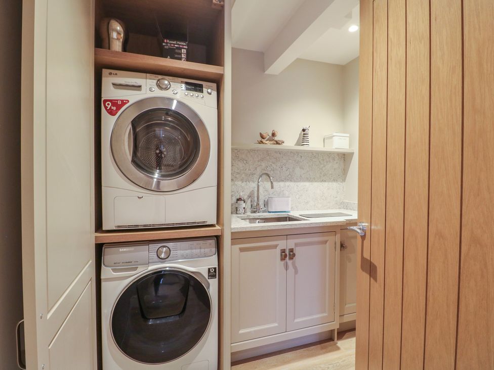 A laundry room with stacked washer and dryer and a sink at The Coach House in Holloway