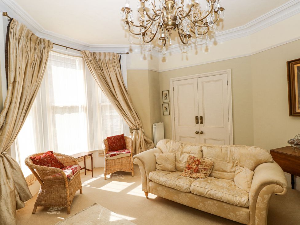 A sitting room with a fabric sofa and two wicker chairs near windows with curtains at Hereford House in Tenby