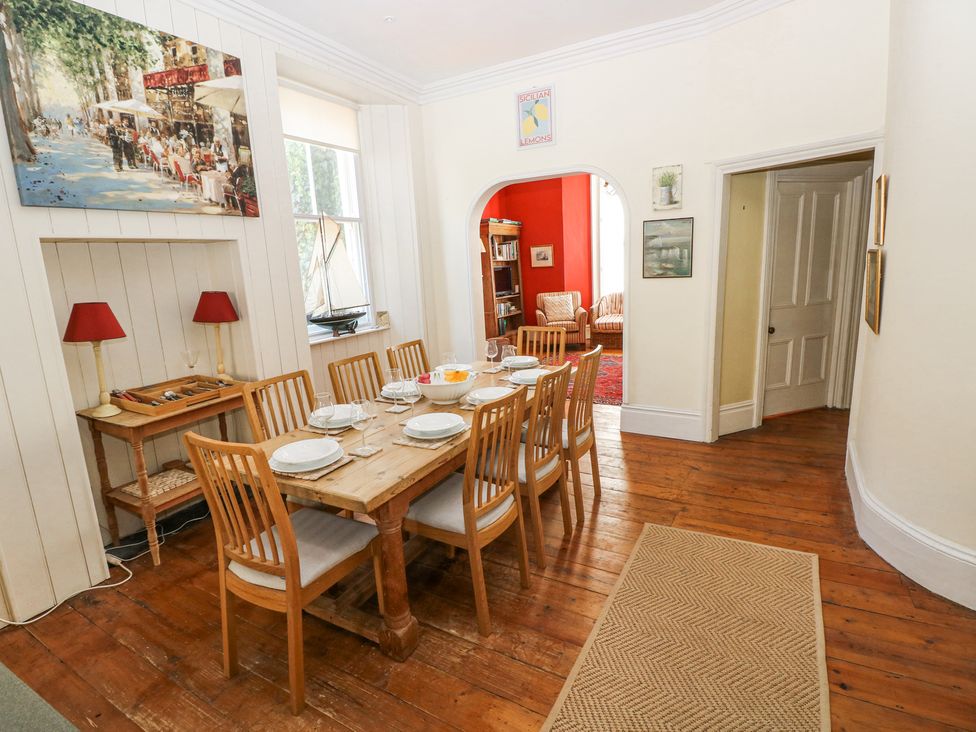 A dining room with a wooden table and eight chairs set with plates and glasses at Hereford House in Tenby