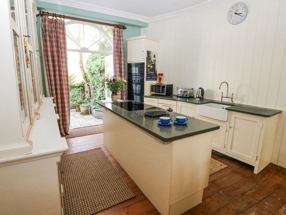 A kitchen with an island countertop with two blue cups and saucers a vase of flowers plaid curtains and a door opening to a garden at Hereford House in Tenby