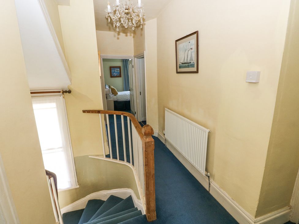 A hallway with a staircase carpeted in blue and a painting on the wall at Hereford House in Tenby