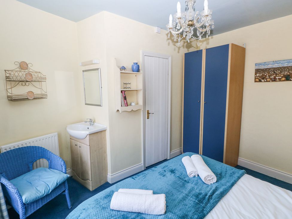 A bedroom with a bed, blue wardrobe, blue chair, small sink, and wall shelves at Hereford House in Tenby