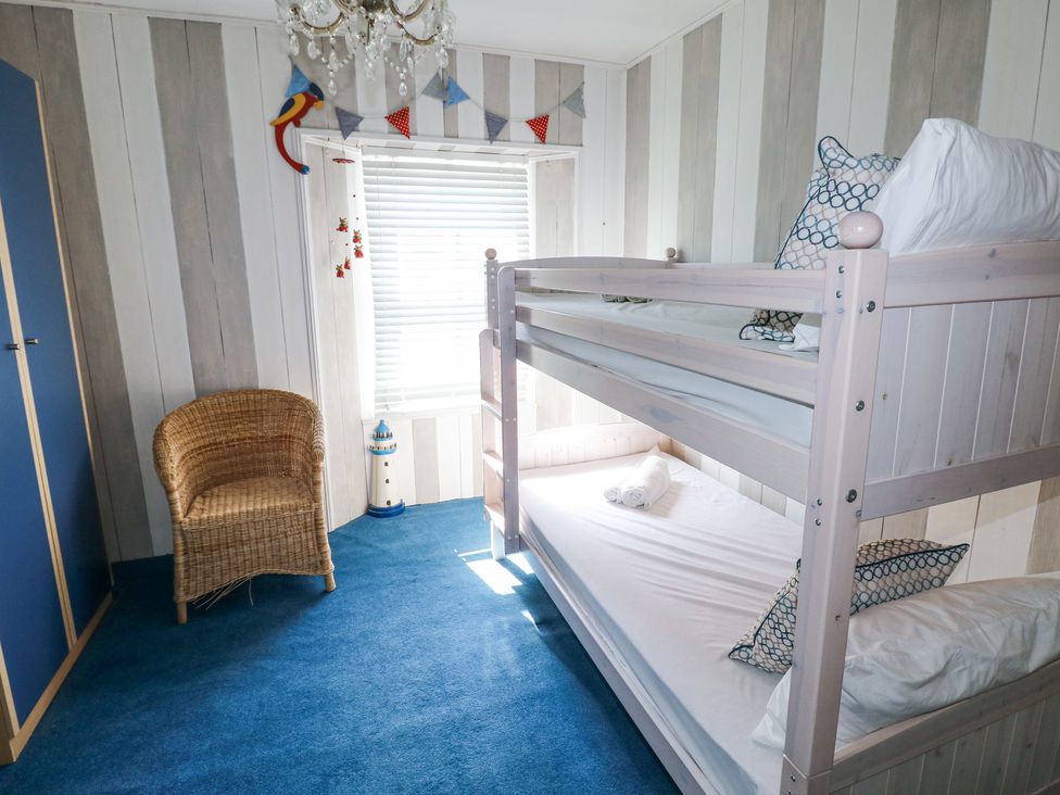 A bedroom with bunk beds a wicker chair a blue carpet and a window with blinds at Hereford House in Tenby