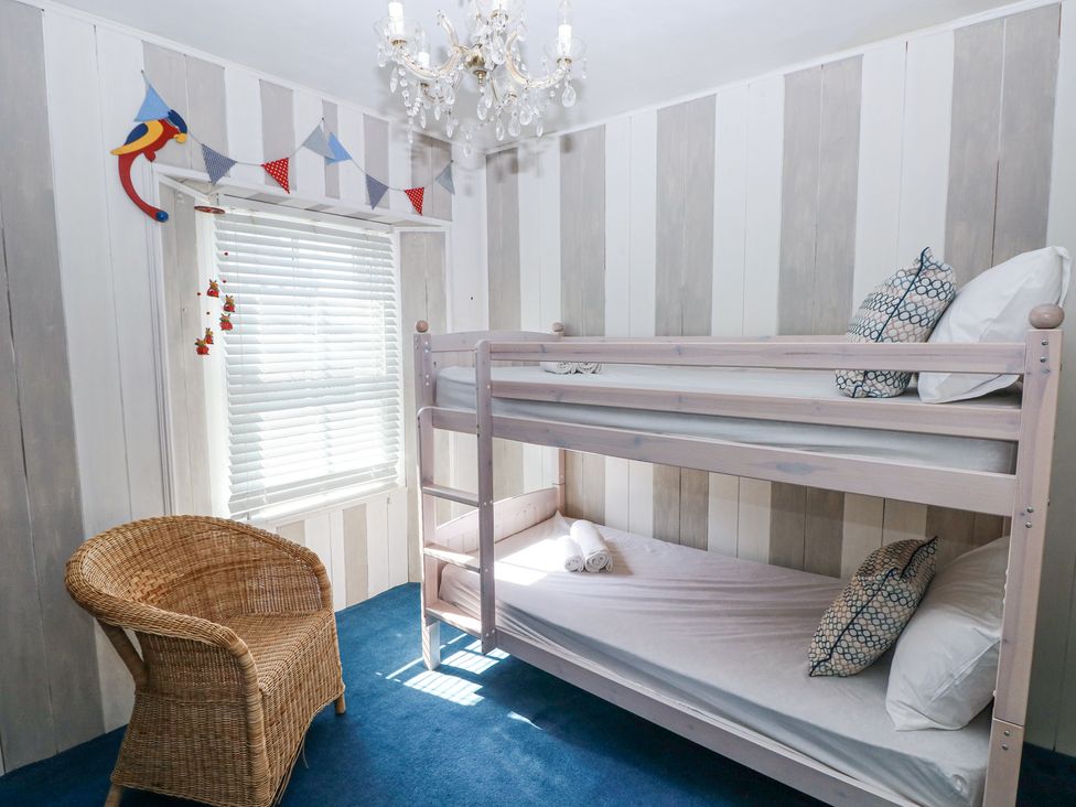 A bedroom with a wooden bunk bed a wicker chair a window with blinds and a chandelier at Hereford House in Tenby