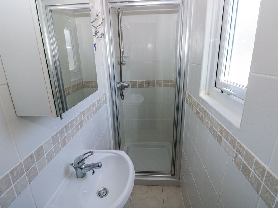 A bathroom with a shower enclosure a washbasin with a faucet a window and a wall-mounted mirror cabinet at Hereford House in Tenby