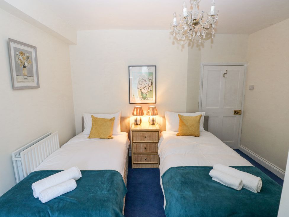 A bedroom with two single beds a side table with lamps and towels at Hereford House in Tenby