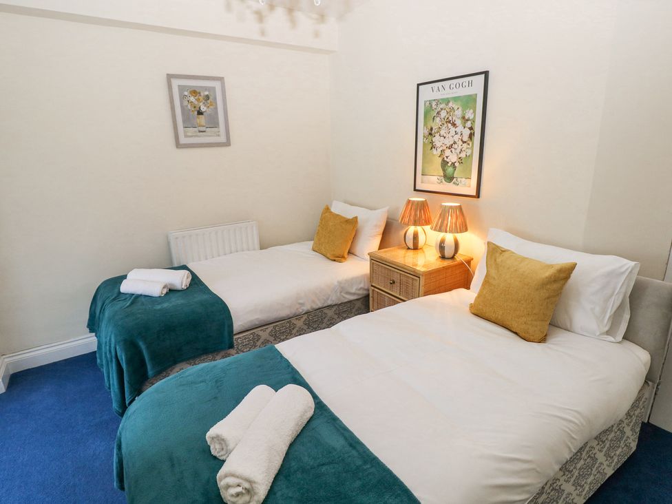 A bedroom with two single beds with yellow cushions and teal throws at Hereford House in Tenby