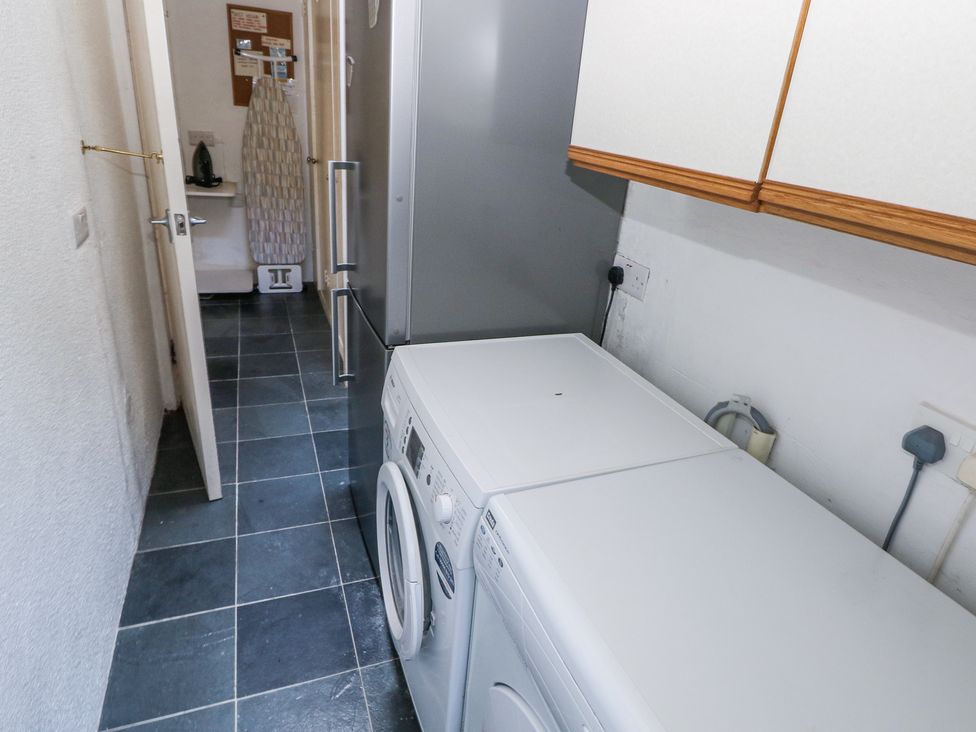 A laundry room with a washing machine ironing board refrigerator and wall cabinets at Hereford House in Tenby