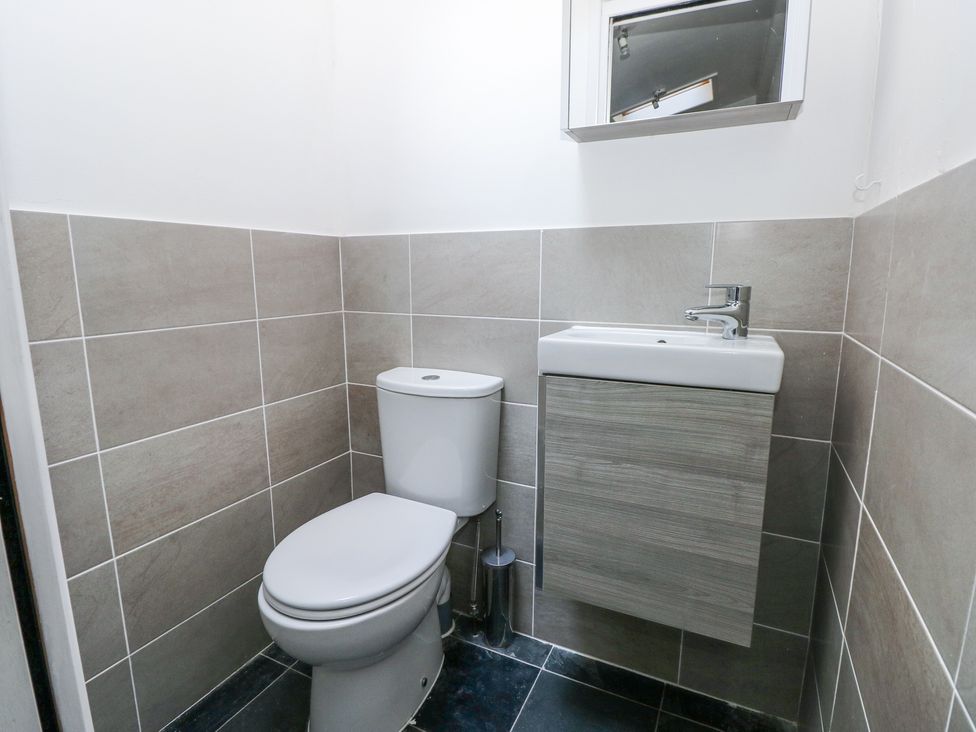 A small bathroom with a white toilet and a wall-mounted sink with a cabinet at Hereford House in Tenby