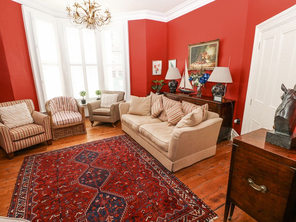 A living room with beige sofa striped armchairs red walls wooden floor and a red patterned rug at Hereford House in Tenby