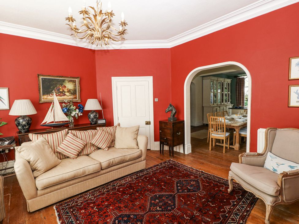 A living room with beige sofa and armchair red walls wooden floor and an archway to a dining room at Hereford House in Tenby