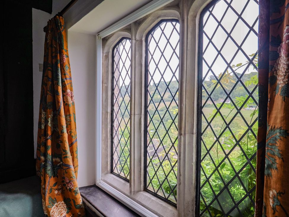 A window with stained glass and floral curtains at Hole House in Branscombe