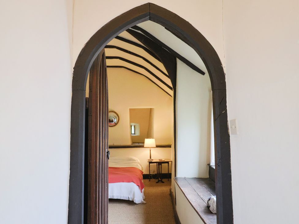 A bedroom with a bed and lamp viewed through an archway at Hole House in Branscombe