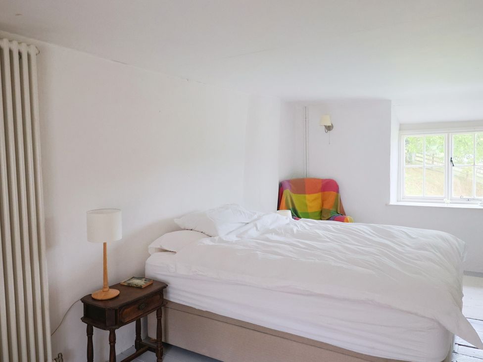 A bedroom with a bed, lamp, and chair at Hole House in Branscombe