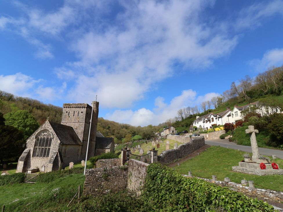 A church with a graveyard and houses in the background at Hole House in Branscombe