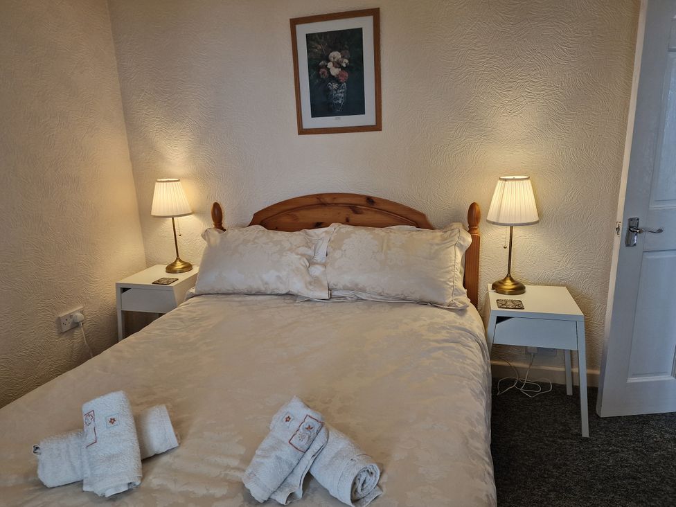 A bedroom with a bed, bedside tables, lamps, and towels at Woodland Roost in Barmouth