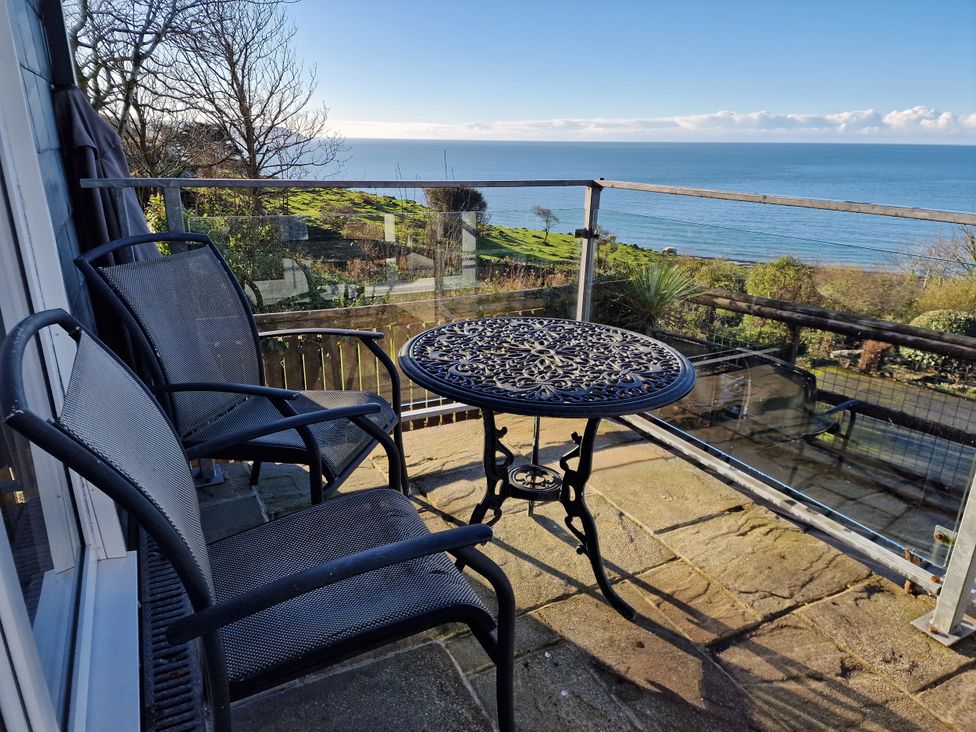 A balcony with table and chairs overlooking the sea at Woodland Roost in Barmouth