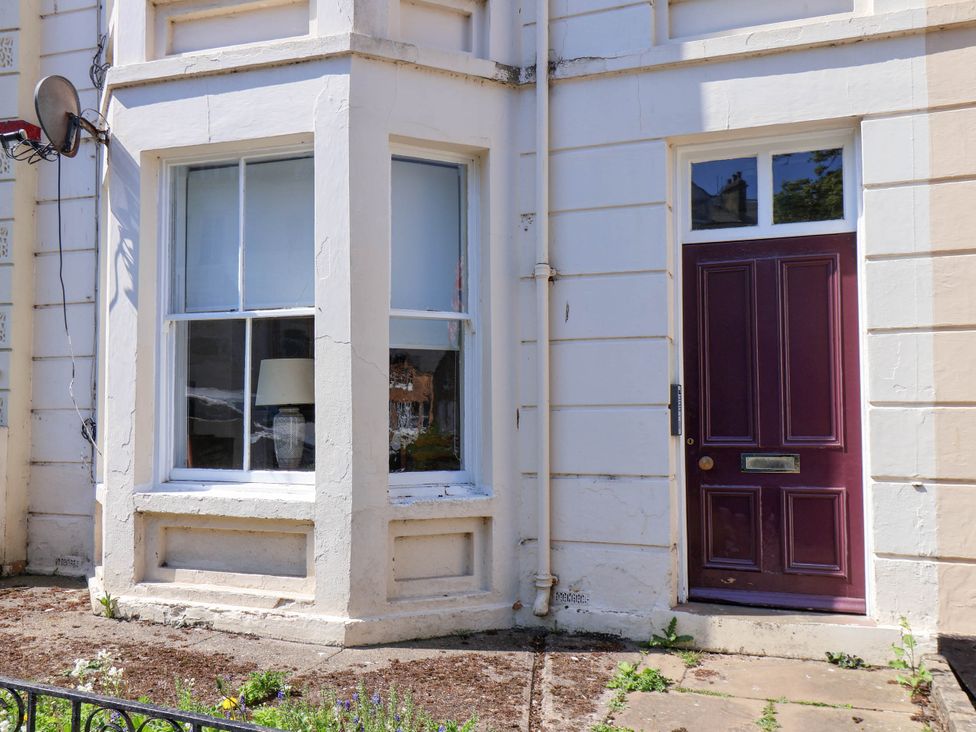 Exterior view of a building showing a window with a lamp inside and a maroon door at Flat 1 in Scarborough